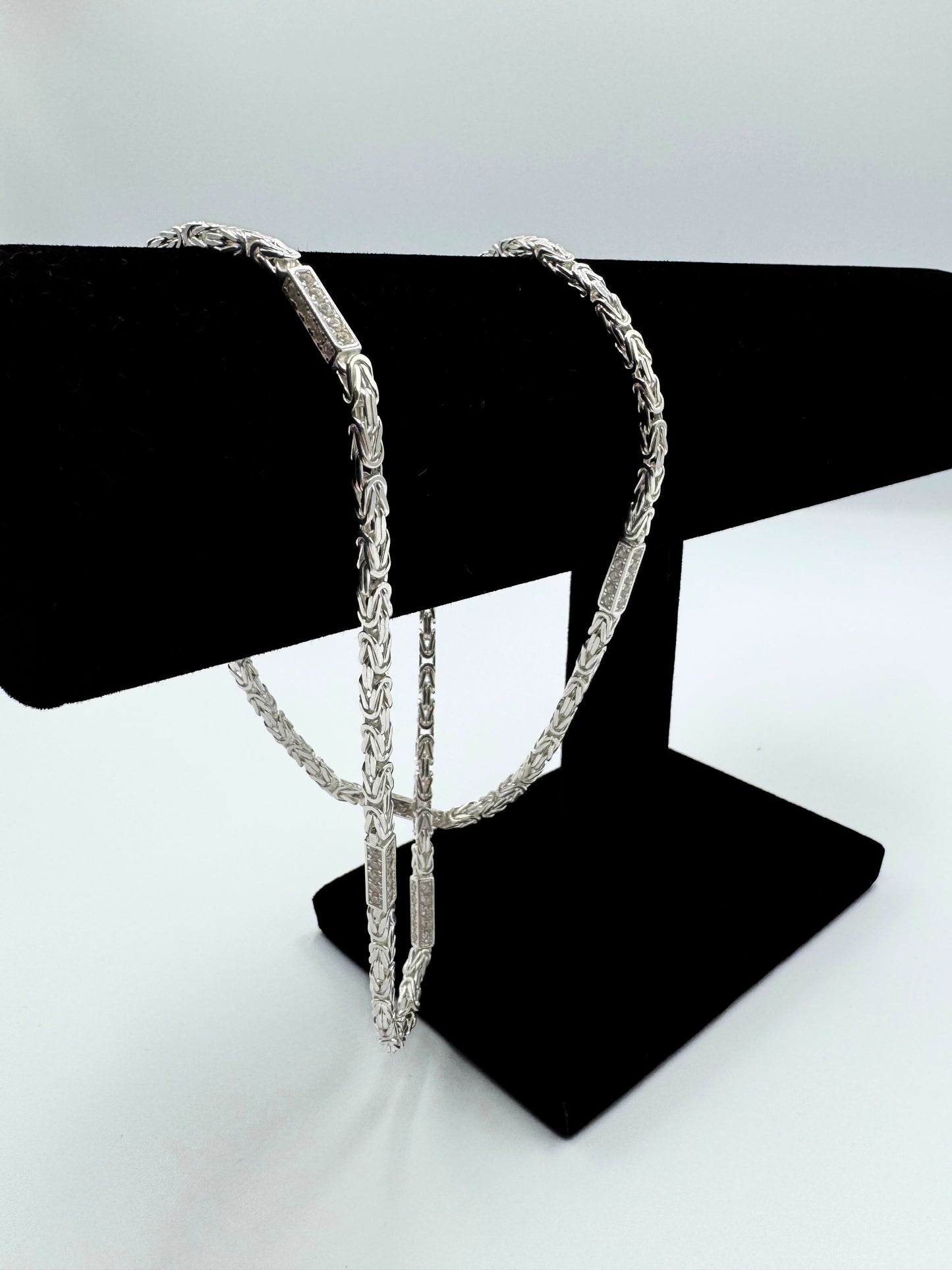 Funkelnde 925er Sterling Silberkette im "Iced Out" Stil, eine luxuriöse Königskette für Herren und Damen. Die Kette ist kunstvoll gearbeitet und mit glitzernden Zirkonia-Steinen besetzt, die für einen auffälligen und edlen Look sorgen. Präsentiert wird die Silberkette auf einem eleganten, schwarzen Samtständer-Schmuckpuppe vor einem klaren, weißen Hintergrund. Diese hochwertige Königskette aus echtem Sterlingsilber ist ein exklusives Schmuckstück, das jedes Outfit aufwertet. Die Kette ist massiv.