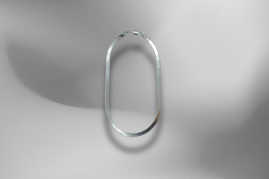 Elegantes 925er Sterling Silber Fischgrätenarmband, schwebend auf einem sanften, grau-schattierten Hintergrund. Das flache, glänzende Silberarmband, eine hochwertige Fischgrätenkette, wird freigestellt präsentiert und wirft einen weichen Schatten auf den monochromen Hintergrund. Hochwertiges Armband, zeitloses Herringbone, flaches Silberarmband, edles Armband, Schmuckstück, Silberarmband, Armband für Herren und Damen, Luxus-Accessoire, elegante Armband, Schmuck-Fotografie.