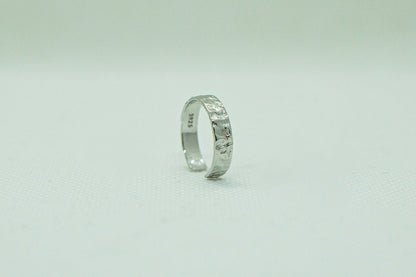 Einzelner, offener Silberring mit gehämmert wirkender Textur, präsentiert auf einem hellen, einfarbigen Hintergrund. Der Ring, mit seiner rustikalen Eleganz und dem einzigartigen Design, ist das zentrale Element des Bildes. Silberring, gehämmert, offener Ring, unisexring, Schmuck, Modeschmuck, Accessoires, handgefertigter Schmuck.