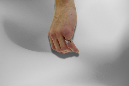 Zwei silberne, gehämmert wirkende Ringe am Finger einer männlichen Hand, präsentiert auf einem sanften, grau-schattierten Hintergrund. Die Ringe, mit ihrer einzigartigen Textur und offenem Design, zeigen eine rustikale Eleganz am Finger. Herrenringe, Silberringe, gehämmert, offene Ringe, Schmuck, Modeschmuck, Accessoires, handgefertigter Schmuck, Ringe an Hand, Schmuck am Model.