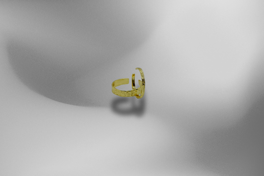 Vergoldeter Silberring mit gehämmert wirkender Textur, präsentiert auf einem sanften, grau-schattierten Hintergrund. Der Ring, mit seiner goldenen Oberfläche und offenem Design, ist das zentrale Element des Bildes. Goldring, Silberring, vergoldet, Damenring, Schmuck, Modeschmuck, Accessoires, handgefertigter Schmuck, grauer Hintergrund.