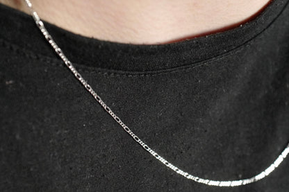 Elegante Figaro-Kette aus 925er Silber mit Diamond-Cut, getragen von einem Live-Model. Die filigranen, polierten Glieder reflektieren das Licht und verleihen der Kette einen edlen Glanz. Durch ihr zeitloses Design ist sie sowohl für Damen als auch Herren geeignet – perfekt für den Alltag oder besondere Anlässe. Ideal als modisches Accessoire oder stilvolles Geschenk.