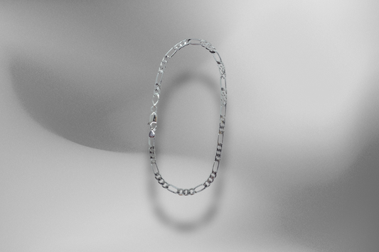 Elegantes 925er Sterling Silber Figaro Armband, schwebend auf einem sanften, grau-schattierten Hintergrund. Das massive Silberarmband, eine hochwertige Figaro-Kette, wird freigestellt präsentiert und wirft einen weichen Schatten auf den monochromen Hintergrund. Hochwertiges Armband, zeitloses Figaro Armband, massive Silberarmband, edles Armband, Schmuckstück, Silberarmband, Armband für Herren und Frauen, Luxus-Accessoire, elegante Armband, Schmuck-Fotografie.