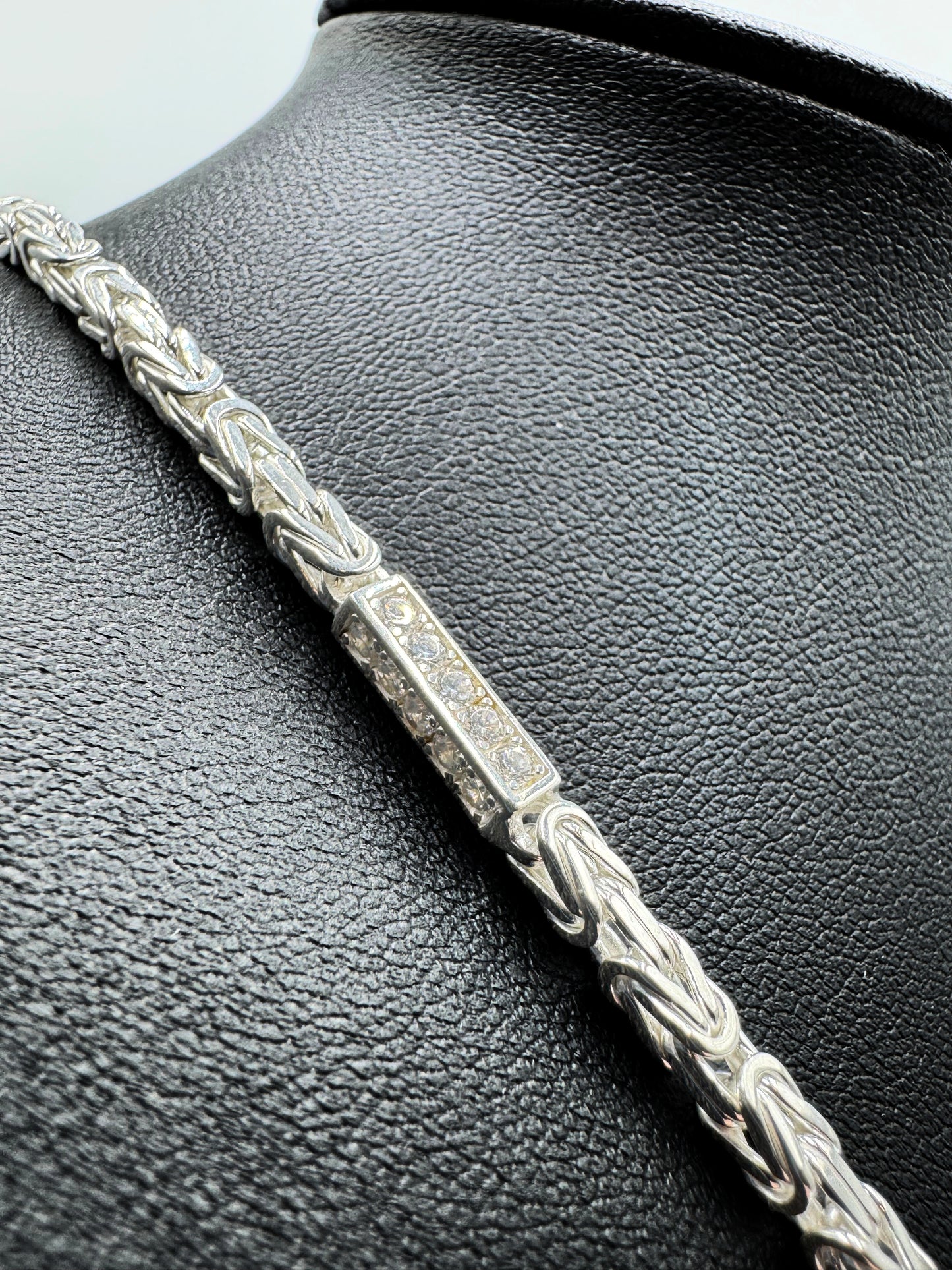 Funkelnde 925er Sterling Silberkette im "Iced Out" Stil, eine luxuriöse Königskette für Herren und Damen. Die Kette ist kunstvoll gearbeitet und mit glitzernden Zirkonia-Steinen besetzt, die für einen auffälligen und edlen Look sorgen. Präsentiert wird die Silberkette auf einer eleganten, schwarzen Leder-Schmuckpuppe vor einem klaren, weißen Hintergrund. Diese hochwertige Königskette aus echtem Sterlingsilber ist ein exklusives Schmuckstück, das jedes Outfit aufwertet. Die Kette ist massiv.