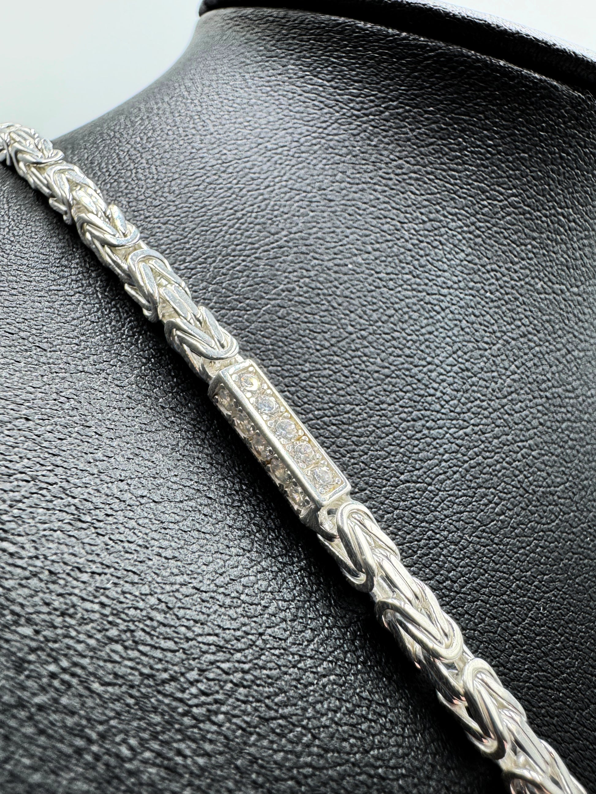 Funkelnde 925er Sterling Silberkette im "Iced Out" Stil, eine luxuriöse Königskette für Herren und Damen. Die Kette ist kunstvoll gearbeitet und mit glitzernden Zirkonia-Steinen besetzt, die für einen auffälligen und edlen Look sorgen. Präsentiert wird die Silberkette auf einer eleganten, schwarzen Leder-Schmuckpuppe vor einem klaren, weißen Hintergrund. Diese hochwertige Königskette aus echtem Sterlingsilber ist ein exklusives Schmuckstück, das jedes Outfit aufwertet. Die Kette ist massiv.