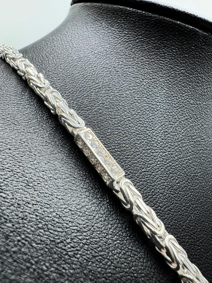 Funkelnde 925er Sterling Silberkette im "Iced Out" Stil, eine luxuriöse Königskette für Herren und Damen. Die Kette ist kunstvoll gearbeitet und mit glitzernden Zirkonia-Steinen besetzt, die für einen auffälligen und edlen Look sorgen. Präsentiert wird die Silberkette auf einer eleganten, schwarzen Leder-Schmuckpuppe vor einem klaren, weißen Hintergrund. Diese hochwertige Königskette aus echtem Sterlingsilber ist ein exklusives Schmuckstück, das jedes Outfit aufwertet. Die Kette ist massiv.