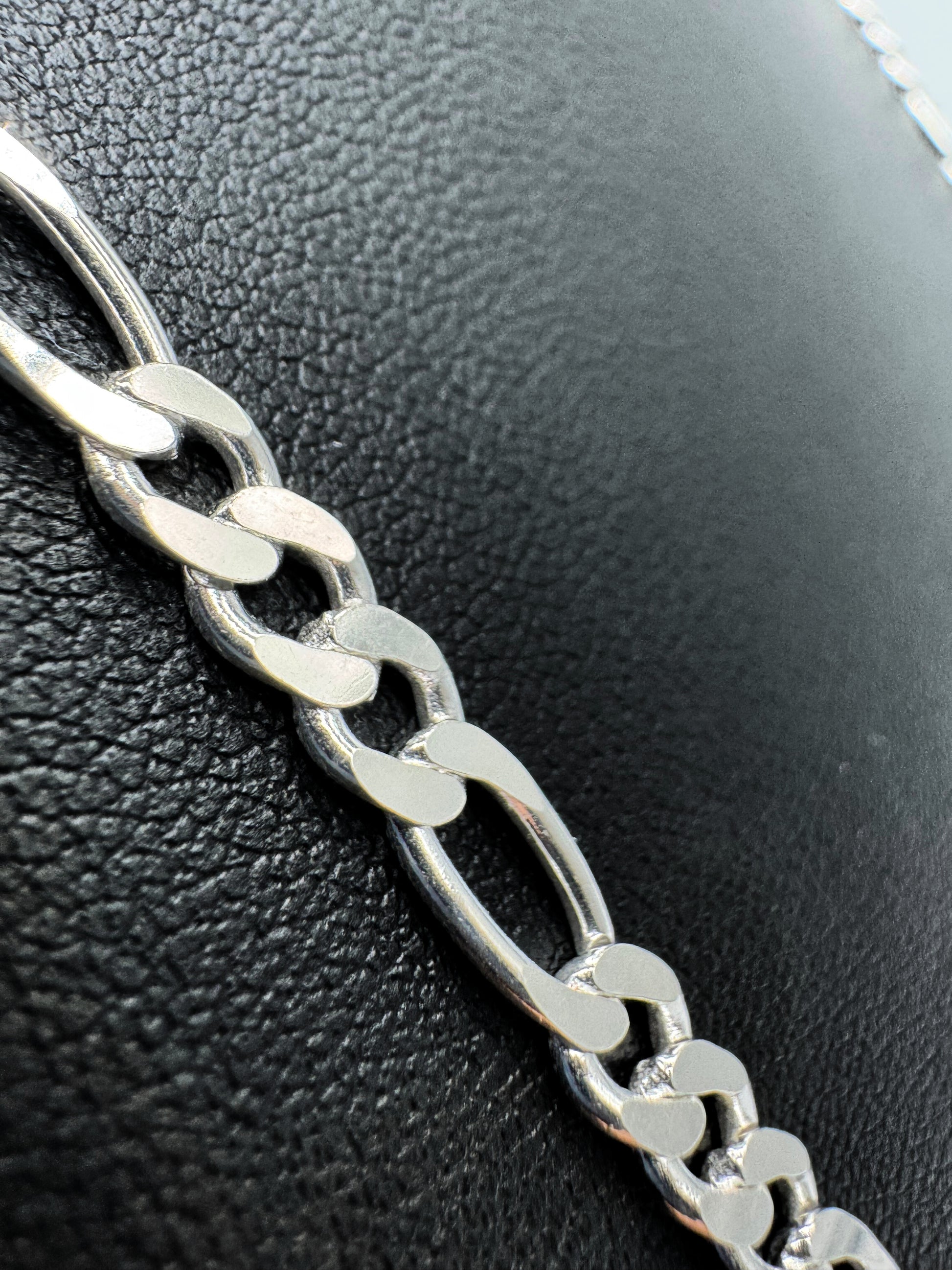Eine silberne Figaro-Kettenhalskette auf einem schwarzen Lederuntergrund. Die Kette hat ein klassisches Design mit abwechselnd großen und kleinen Gliedern, ideal für den Alltag oder als elegantes Accessoire. Für Mann und Frau geeignet (Unisex). 