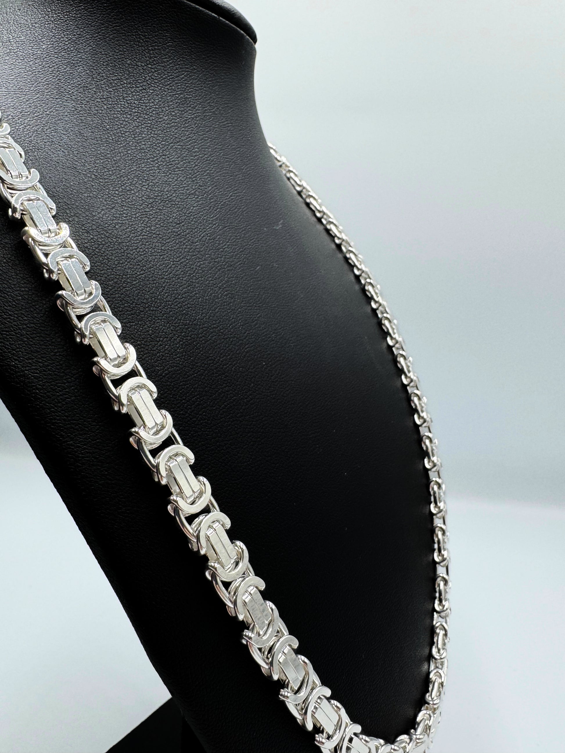 Massive 925er Sterling Silber Königskette, ein zeitloses Schmuckstück für Herren. Die Kette besticht durch ihre robuste Verarbeitung und das kunstvolle Design, typisch für eine hochwertige Königskette.  Das glänzende Sterlingsilber sorgt für einen edlen Look. Die Kette wird auf einer eleganten, schwarzen Schmuckpuppe vor einem neutralen, weißen Hintergrund präsentiert, um die Details optimal hervorzuheben. Diese Königskette ist ein Statement-Piece, das jedem Outfit einen Hauch von Luxus verleiht.