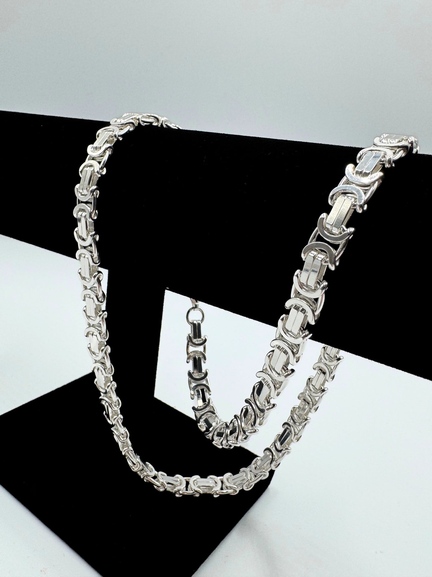 Massive 925er Sterling Silber Königskette, ein zeitloses Schmuckstück für Herren. Die Kette besticht durch ihre robuste Verarbeitung und das kunstvolle Design, typisch für eine hochwertige Königskette.  Das glänzende Sterlingsilber sorgt für einen edlen Look. Die Kette wird auf einer eleganten, schwarzen Schmuckpuppe vor einem neutralen, weißen Hintergrund präsentiert, um die Details optimal hervorzuheben. Diese Königskette ist ein Statement-Piece, das jedem Outfit einen Hauch von Luxus verleiht.