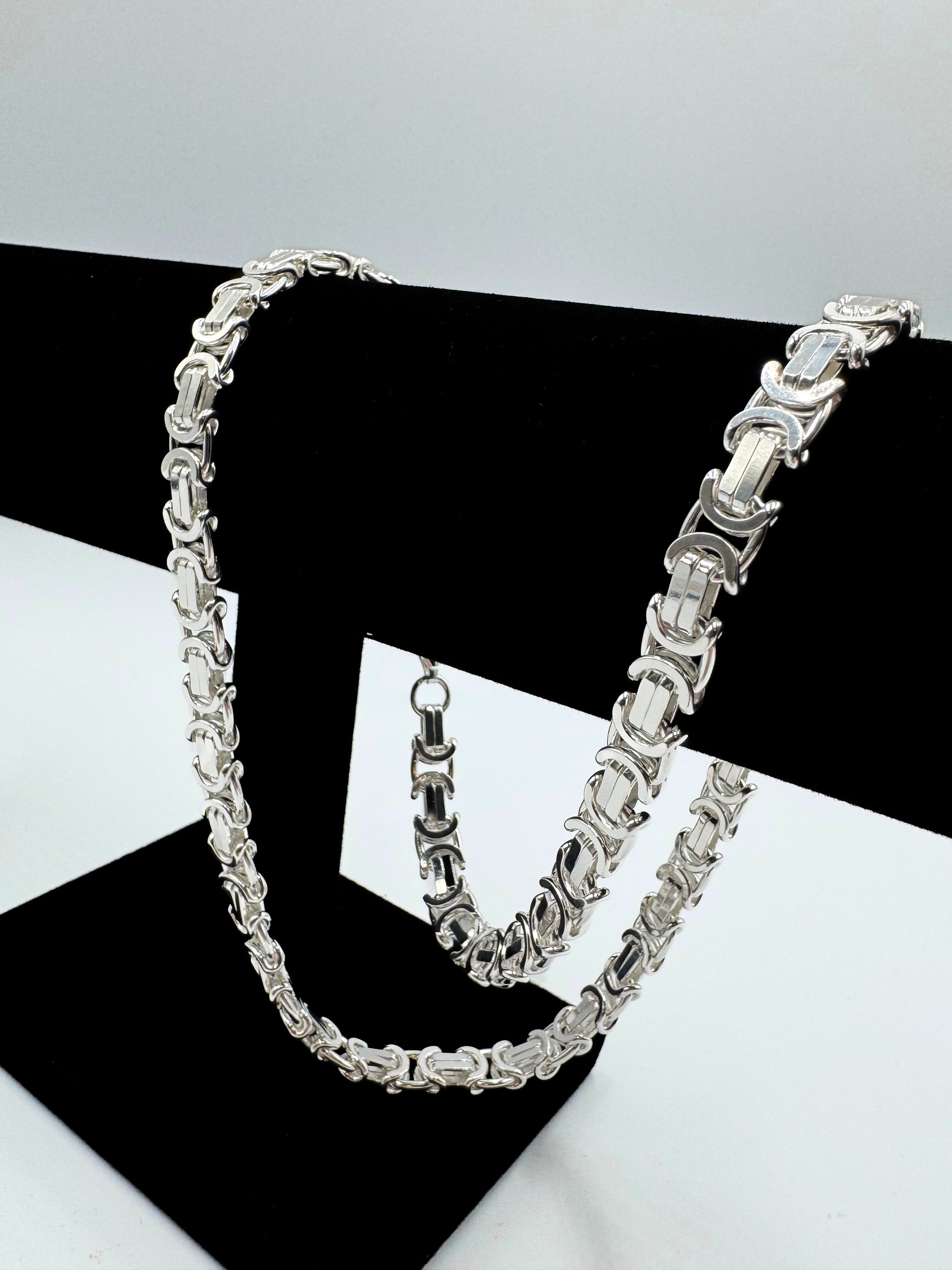 Massive 925er Sterling Silber Königskette, ein zeitloses Schmuckstück für Herren. Die Kette besticht durch ihre robuste Verarbeitung und das kunstvolle Design, typisch für eine hochwertige Königskette.  Das glänzende Sterlingsilber sorgt für einen edlen Look. Die Kette wird auf einer eleganten, schwarzen Schmuckpuppe vor einem neutralen, weißen Hintergrund präsentiert, um die Details optimal hervorzuheben. Diese Königskette ist ein Statement-Piece, das jedem Outfit einen Hauch von Luxus verleiht.