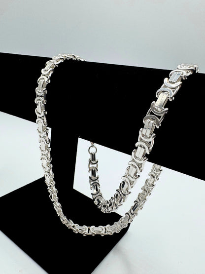 Massive 925er Sterling Silber Königskette, ein zeitloses Schmuckstück für Herren. Die Kette besticht durch ihre robuste Verarbeitung und das kunstvolle Design, typisch für eine hochwertige Königskette.  Das glänzende Sterlingsilber sorgt für einen edlen Look. Die Kette wird auf einer eleganten, schwarzen Schmuckpuppe vor einem neutralen, weißen Hintergrund präsentiert, um die Details optimal hervorzuheben. Diese Königskette ist ein Statement-Piece, das jedem Outfit einen Hauch von Luxus verleiht.