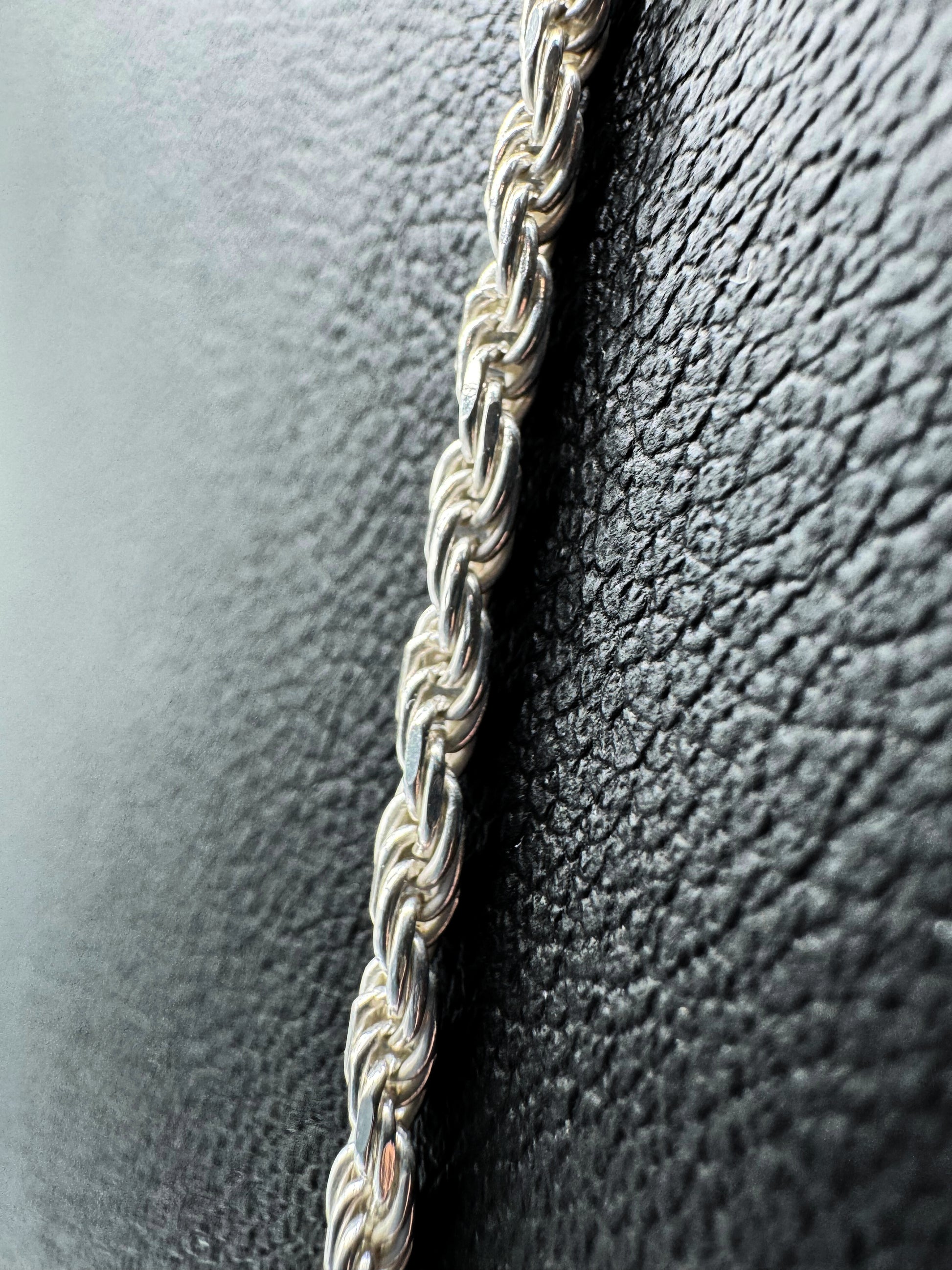 Detailaufnahme einer hochwertigen Kordelkette aus 925er Sterlingsilber – fein geflochtenes, robustes Design mit glänzendem Finish. Zeitlose Unisex-Silberkette für Damen und Herren, elegant präsentiert auf strukturiertem schwarzem Hintergrund